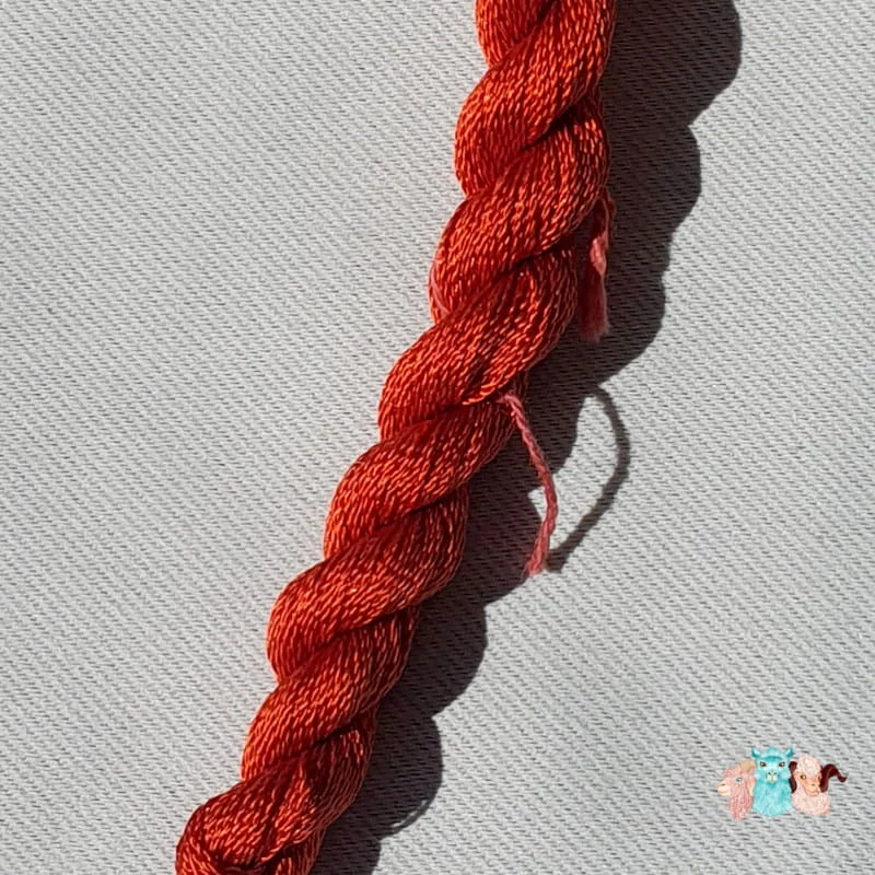 Détail d'un écheveau de fil de soie orange foncé avec des fleurs sur fond gris, fabriqué en france