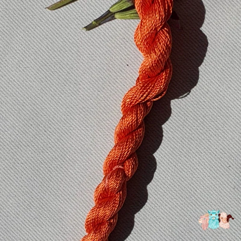 Détail d'un écheveau de fil de soie orange moyen avec des fleurs sur fond gris, fabriqué en france