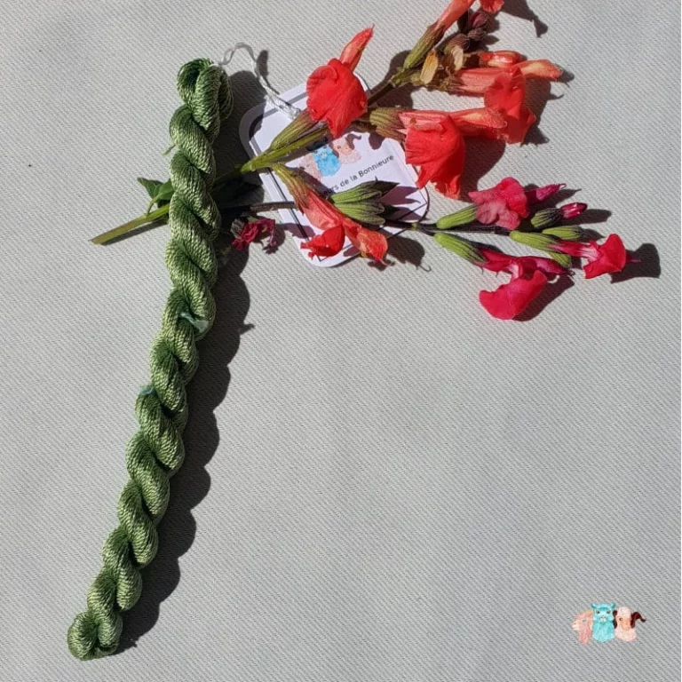 Echeveau de fil de soie vert clair avec des fleurs rouge sur fond gris, fabriqué en france