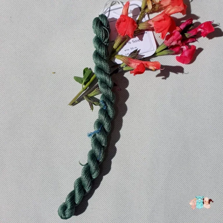 Echeveau de fil de soie vert foncé avec des fleurs rouge sur fond gris, fabriqué en france