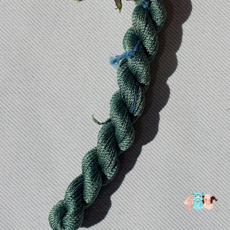 Détail d'un écheveau de fil de soie vert foncé sur fond gris, fabriqué en france