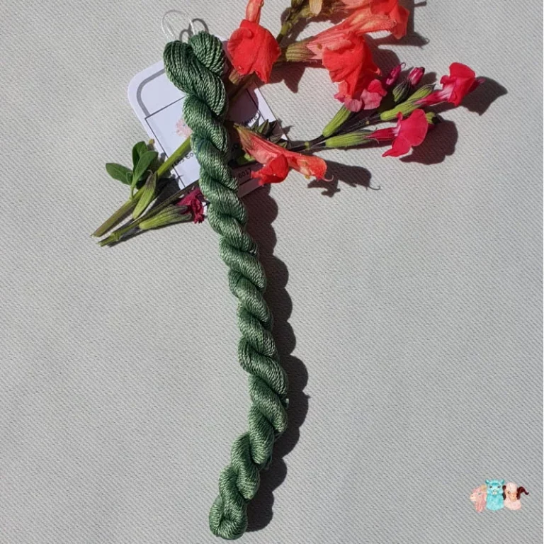 Echeveau de fil de soie vert moyen avec des fleurs rouge sur fond gris, fabriqué en france