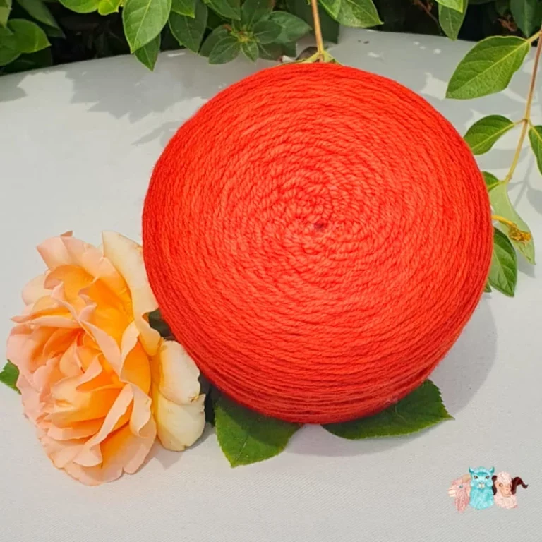 Echeveau et pelote de laine de coloris de l'orange foncé à l'orange rouge clair devant des feuilles vertes et posé sur