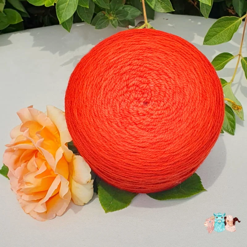 Echeveau et pelote de laine de coloris de l'orange foncé à l'orange rouge clair devant des feuilles vertes et posé sur