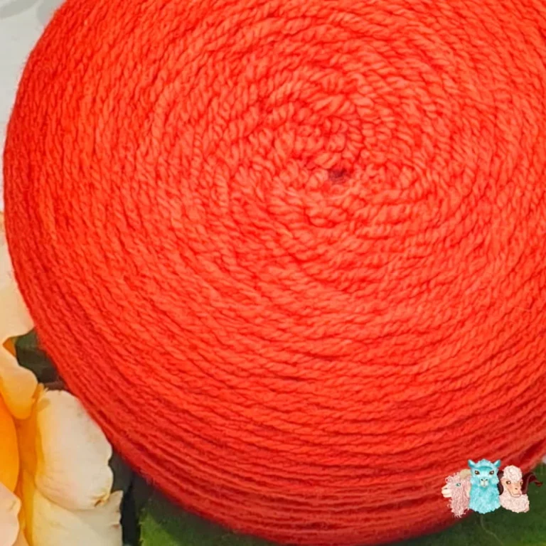 Gros plan d'une pelote de laine de coloris de l'orange foncé à l'orange rouge clair devant des feuilles vertes.