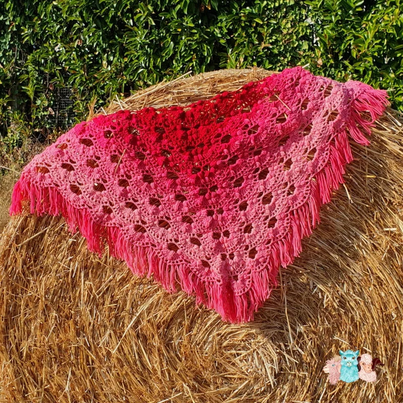 Châle avec des franges en dégradé rouge sur un botte de paille.