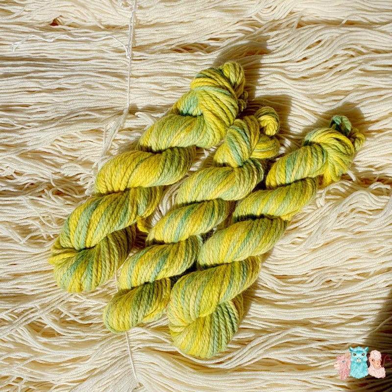 3 Echeveaux de laine mérinos alpaga teinté en jaune et vert sur un fond de fil de laine.
