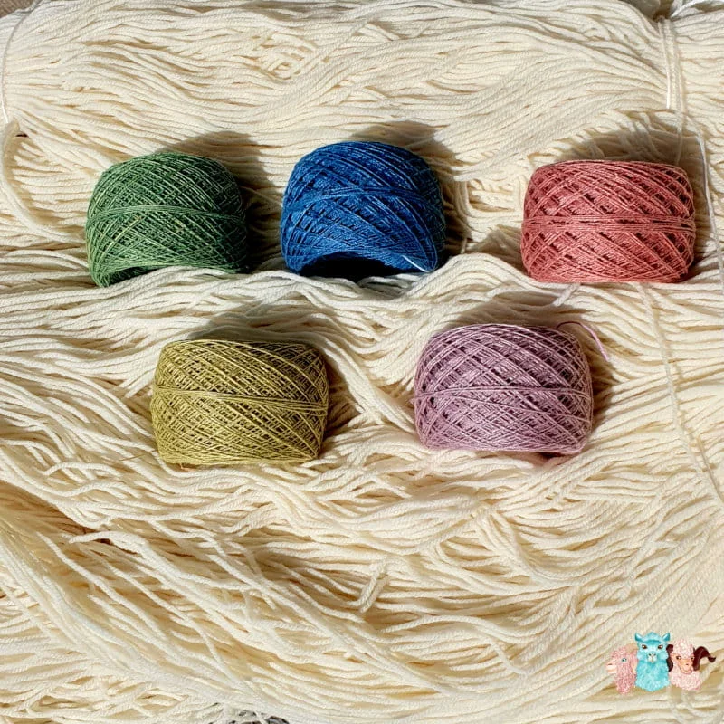 Fils de lin teints avec des colorants naturels, vert, bleu, orange, jaune et violet sur un fond de fil de laine.